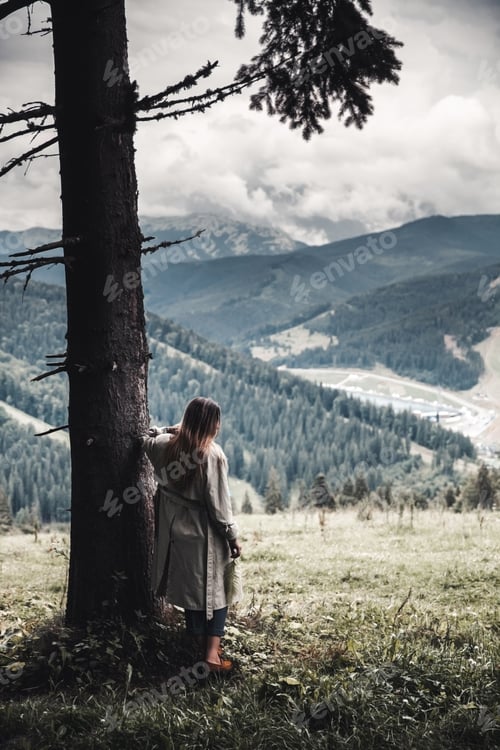 Preview: Beautiful woman in a beige raincoat in the mountains in a forest area. Nature fashion