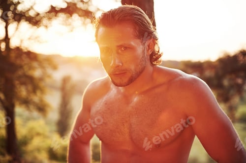 Preview: Handsome shirtless man with muscular body type is in the forest at daytime