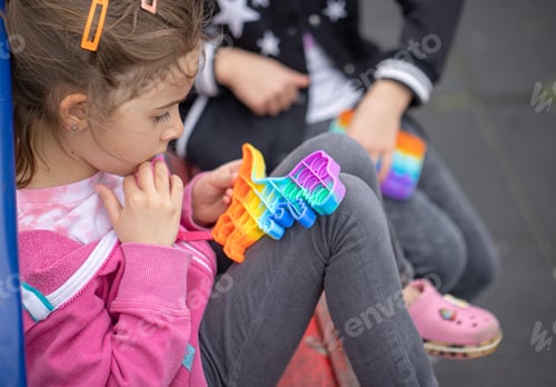 Preview: A little cheerful girl plays with a popular colorful toy antistress pop it.
