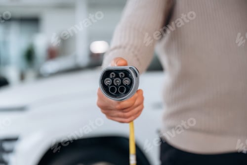 Preview: Conception of ecology, holding charging cable. Man is with the car in dealership