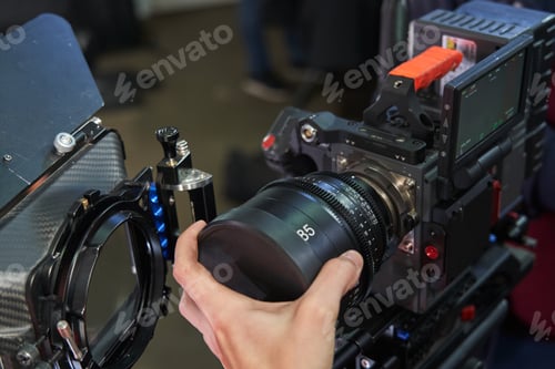 Preview: A caucasian videographer's hand installs an 85mm lens on a professional movie camera