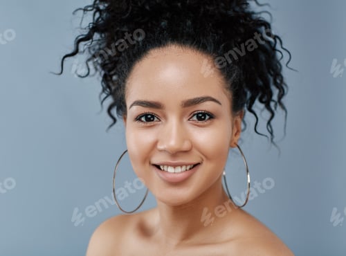 Preview: Portrait of a smiling female with curly hair and earrings looking at camera over blue backdrop