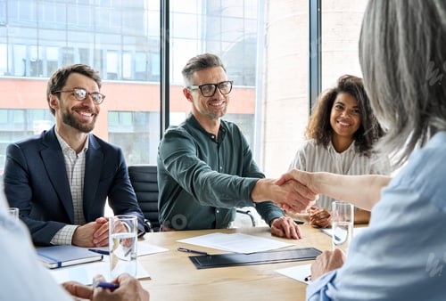 Preview: Happy businessman and businesswoman shaking hands at group meeting.
