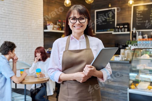 Preview: Portrait of a middle aged woman owner or worker of coffee shop, inside a bakery