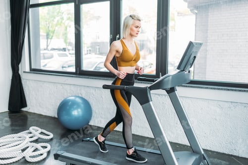 Preview: side view of young sportswoman running on treadmill at gym