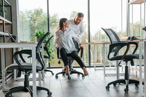 Preview: Having fun by riding the chair. Man and woman are working in the modern office together