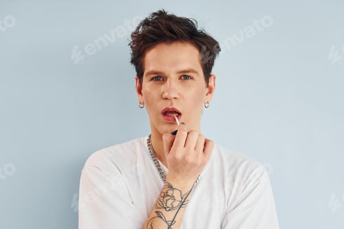 Preview: Young gay man is standing in the studio and posing for a camera. Red colored lips