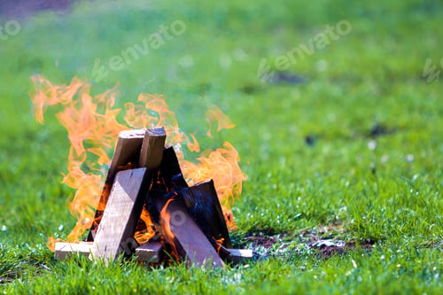 Preview: Glowing bonfire on nature. Burning wooden planks outside on summer day. Bright orange flames, light