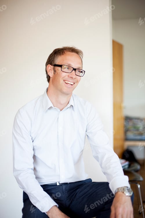 Preview: Happy mature man sitting against white wall at home