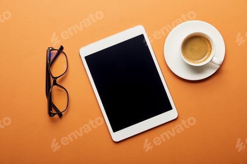 Preview: top view of digital tablet with blank screen near cup of coffee and glasses on orange