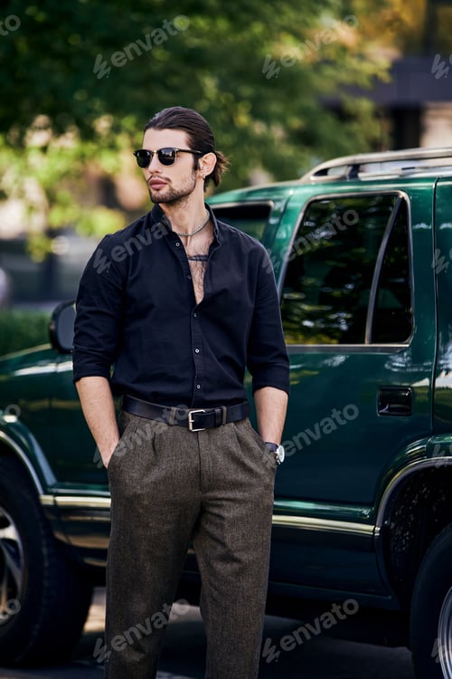 Preview: sexy man with accessories in stylish attire standing next to his car with hands in pockets
