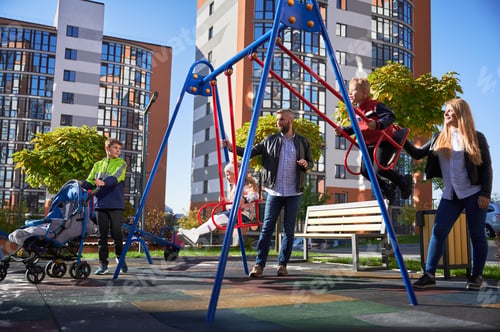 Preview: Happy family - father, mother and children having fun together on playground.