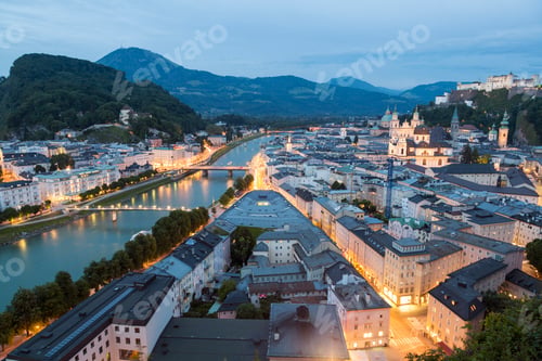 Preview: High angle view across rooftops of city on a river, castle on mountains in the distance.