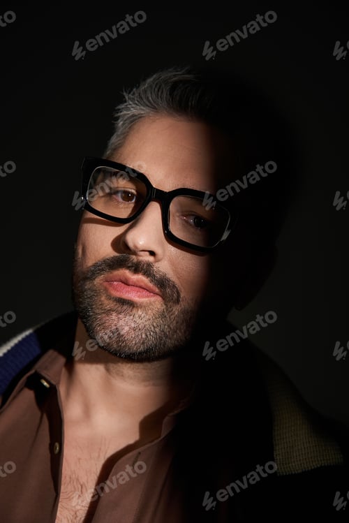 Preview: Stylish man exudes elegance in trendy glasses against a dramatic backdrop in studio