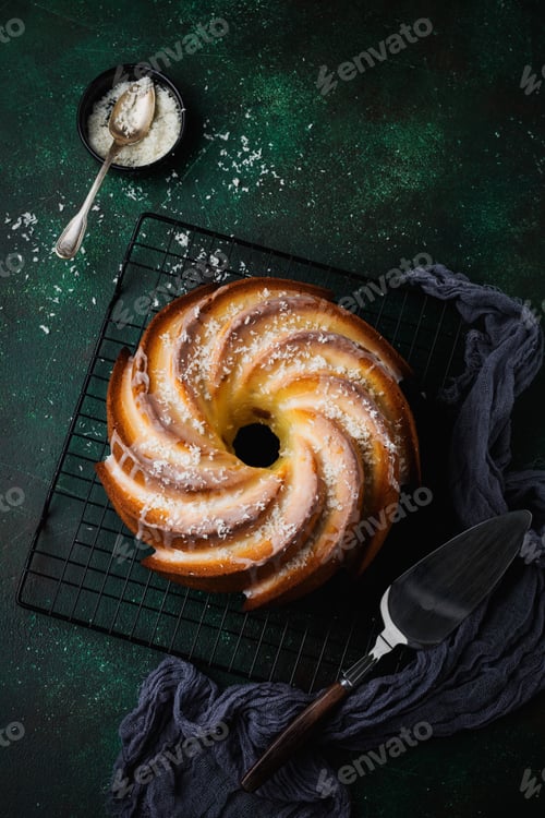 Preview: Bundt cake with sugar glaze and coconut on dark green old concrete background. Selective focus. Top