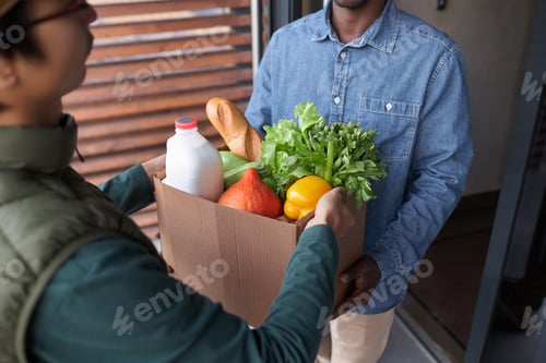 Preview: Close up of delivery guy handing bag with fresh groceries