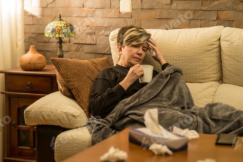 Preview: Woman drinking warm tea to help her with her cold, used tissues in the foreground