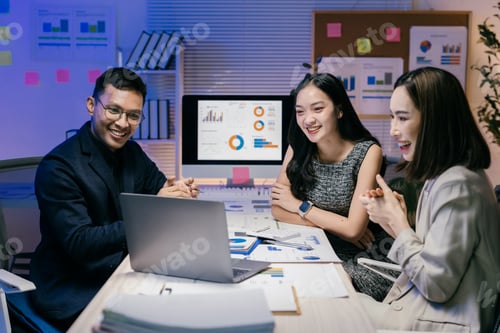 Preview: Group of happy businesspeople discussing strategy using laptop and desktop computer in modern office