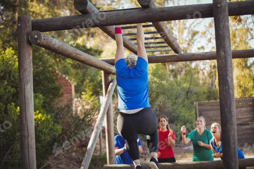 Preview: Woman being cheered bye her teammates to climb monkey bars during obstacle course training