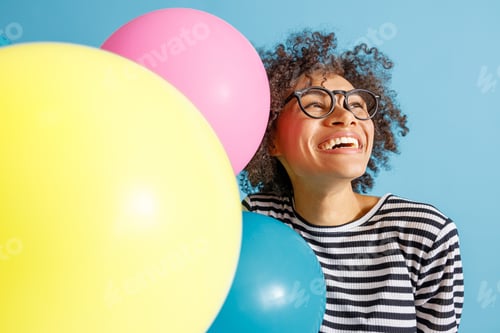 Preview: Cheerful African woman with colorful balloons standing in studio