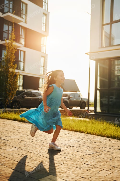 Preview: Cheerful little girl walking outdoors in the city in dress