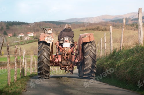 Preview: Female farmer driving tractor on country road near farm in rural landscape