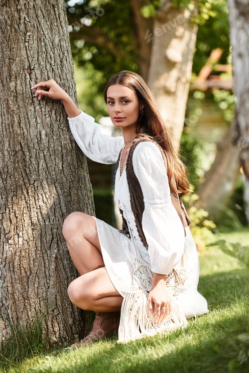 Preview: Young beautiful woman posing gracefully by a tree in a serene garden setting