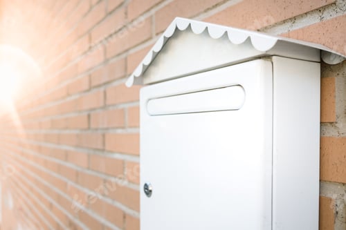 Preview: White mailbox on the brick wall of a house, with an unfocused background and a flare of the sun.