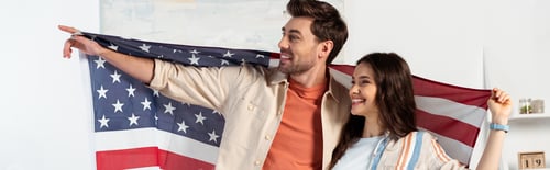Preview: Panoramic crop of smiling man pointing with finger while holding with girlfriend american flag