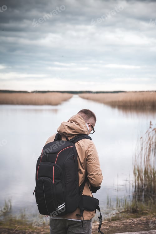 Preview: Vertical shot of a male with a backpack near a lake