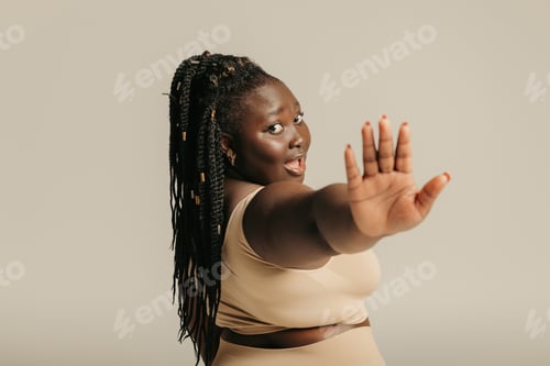 Preview: Rear view of curvy African woman in sportswear stretching out hand on studio background
