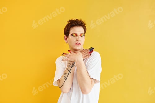 Preview: Young gay man is standing in the studio and posing for a camera. Against yellow background