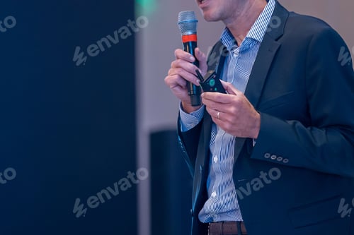 Preview: Male speaker in business suit holding microphone - concept of talk show, motivational speaking