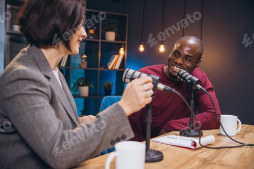 Preview: Two smiling podcasters, a woman and a man, recording an interview in a professional studio