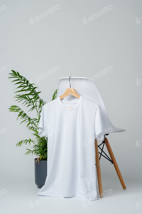 Preview: White blank t-shirt hanging on chair in empty room