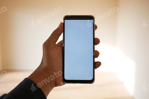 Preview: A person holding a smartphone with a blank screen in a welllit room, showing modern digital usage