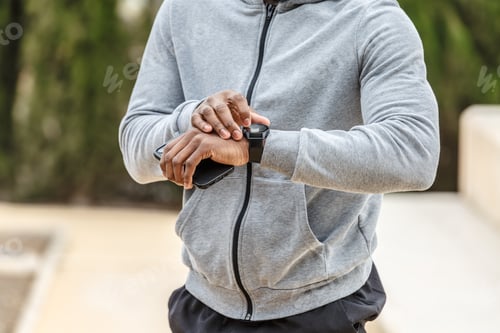 Preview: Crop anonymous African American male athlete in sportswear checking pulse on smart watch while