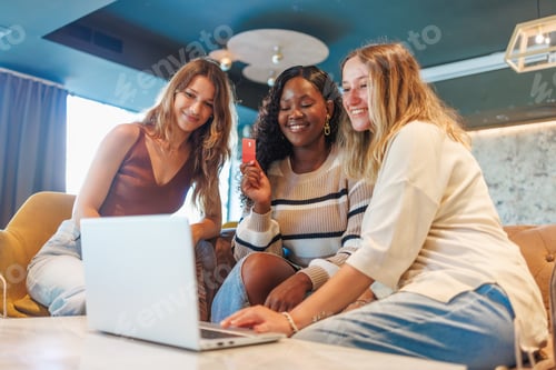 Preview: Three diverse women smiling, using a laptop and credit card for online shopping