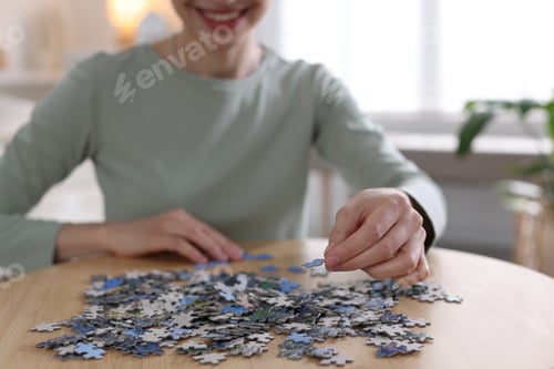 Preview: Woman solving puzzle at wooden table indoors, closeup