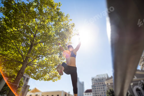 Preview: Athletic woman leaping and holding arms up in the air in the city