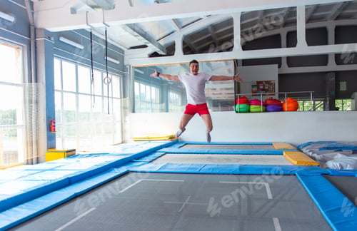 Preview: Fitness, fun, leisure and sport activity concept - Handsome happy man jumping on a trampoline