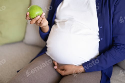 Vista previa: Una
mujer negra milenaria con una gran barriga disfruta del embarazo, sostiene una manzana verde, de cerca. Cuidado de la salud