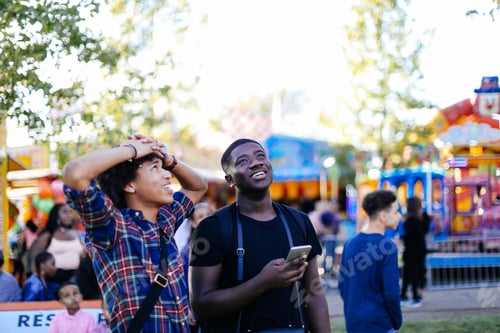 Preview: Two friends at funfair, looking up, laughing