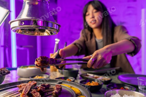 Preview: couple in love having dinner in a Korean restaurant picking up juicy meat from the grill with tongs