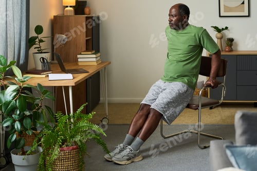 Preview: Senior Black Man Exercising Triceps Dips on Chair in Home Office