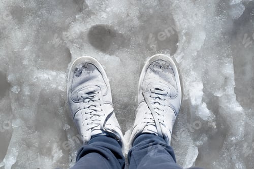 Preview: Feet in wet sneakers standing in the melted snow. Puddles, thaw, muddy underfoot on the sidewalk