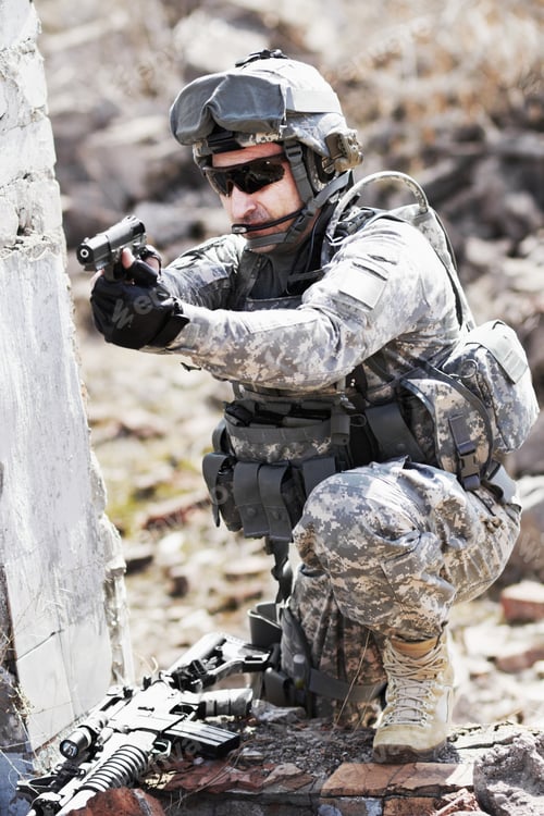 Preview: A soldier crouched down next to a broken down wall and pointing his gun into the distance