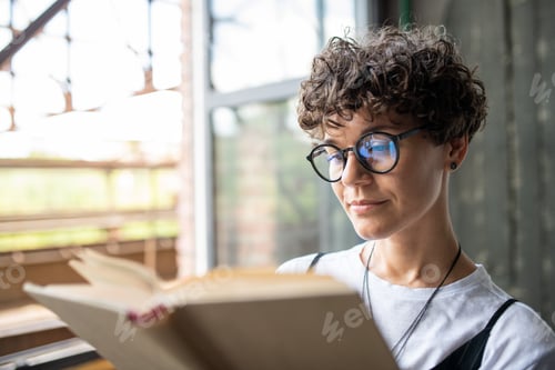 Preview: Young serious woman with brown curly hair looking through pages of novel