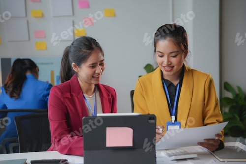 Preview: Two young businesswomen smiling and collaborating on a project using a digital tablet