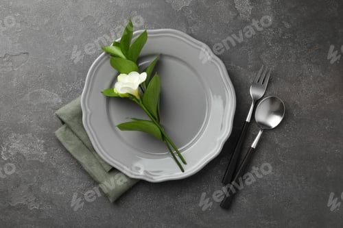 Preview: Stylish setting with cutlery, napkin, flower and plate on grey textured table, flat lay